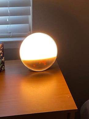 Clock with light on Round alarm clock with upper three quarters light with white light and orange lighted numerals giving the time at the bottom.