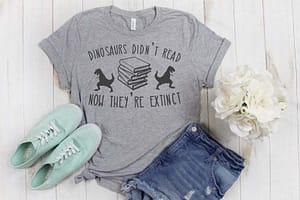 Dinosaurs_Didn't_Read Gray t-shirt on white boards with a pair of jeans and pale green sneakers