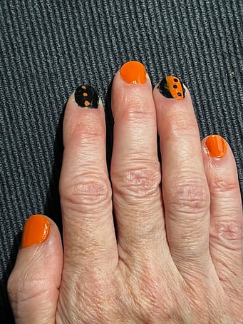 Halloween nails right hand A photo of a right hand with fingernails painted orange or black with an orange design for Halloween