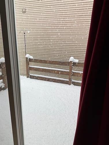 Snow Deck Photo out a tall, sliding window showing a deck covered in snow with snow falling