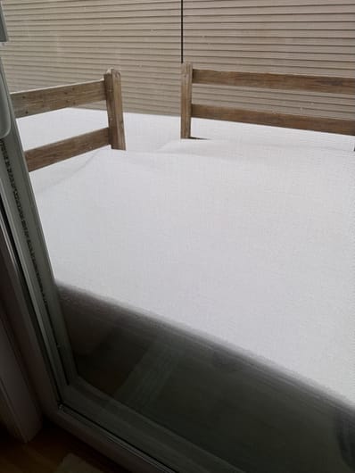 A deck covered with several feet of snow that is visible through the picture window.