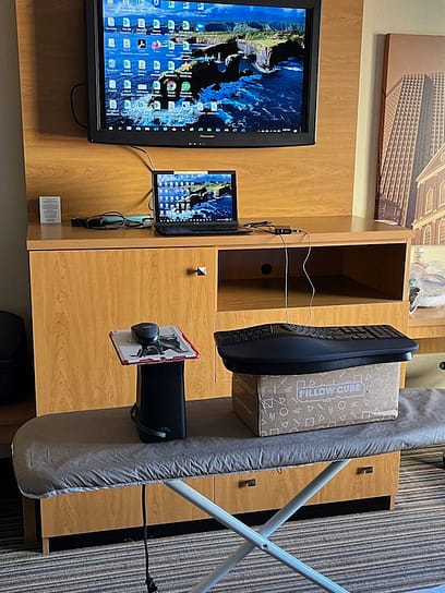 Ironing Board Desk Photo of an ironing board with a computer mouse and keyboard on top. It faces a flat screen tv above a dresser.