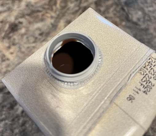 Not Dirty Milk Photo of the top opening of a beverage carton showing a dark liquid inside.