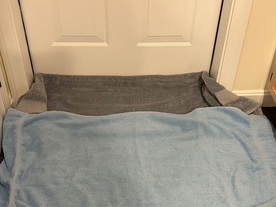 The bottom of a white door blocked by a grey towel and a blue towel.
