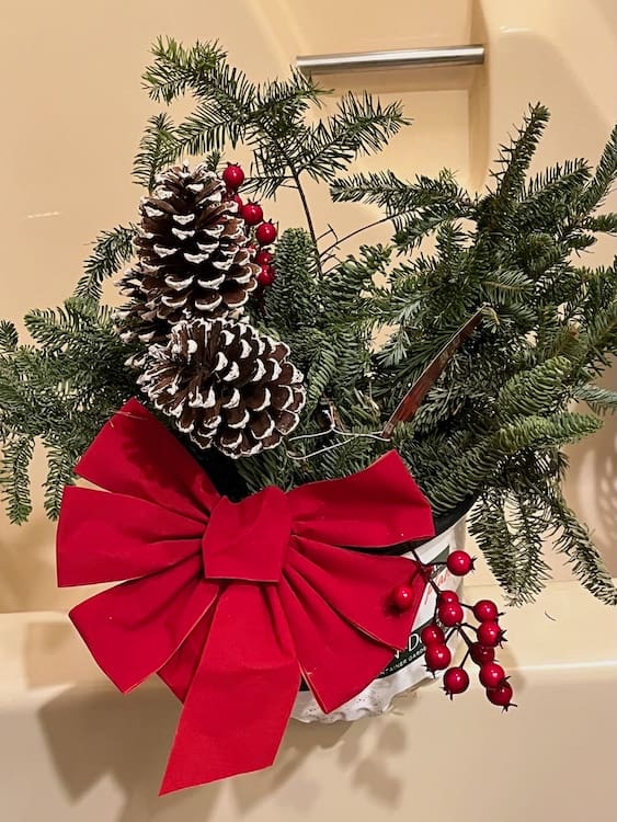 Cannibalized Evergreens Evergreen branches in a decorative display with a red bow, pinecones, and red berries.