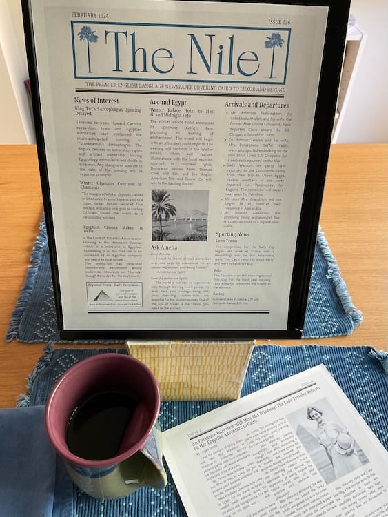 The Nile Photo of a sheet of paper with the title The Nile in blue. The rest of the text is formatted in three columns, with one square photograph in the middle column. The paper rests on a document holder sitting on top of a tissue box. A cup of coffee and the second page of the newspaper are in the foreground.