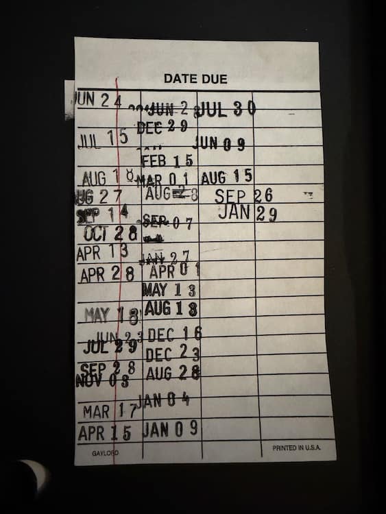 A sheet of paper with horizontal lines and vertical lines marking columns. Library due dates are stamped in several columns.
