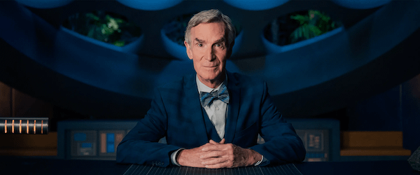 Bill_Nye Photo of Bill Nye staring at the camera. he is wearing a medium blue jacket, a light blue shirt, and a blue patterned bow tie.