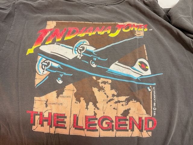 Indy T-Shirt Back A dual-propellor prop plane flies over a sepia toned map. Red text says Indiana Jones The Legend.
