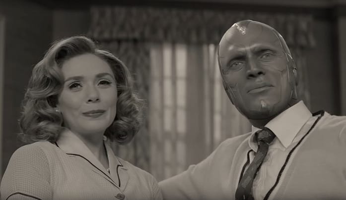 wandavision2 A black and white image of a white woman with crimped chin length hair and a man who is dark skinned with geometric markings on his face