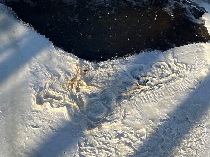 Figure in Foam Photo of sunlight revealing a figure-like shape seemingly carved into frozen foam on top of water.