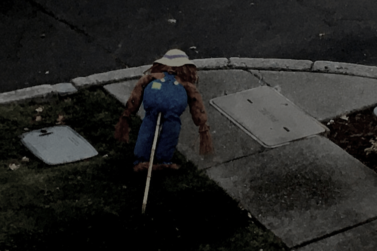 Photo taken from above, in a dark setting, of a figure in a floppy straw hat and blue pants face down as if in a pushup position