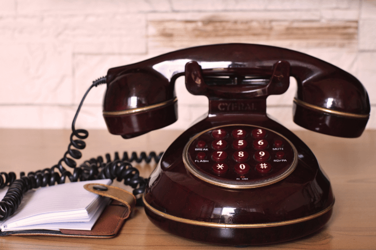 Photo of an open diary in a leather cover on the left with an old-fashioned telephone with push buttons on the right.
