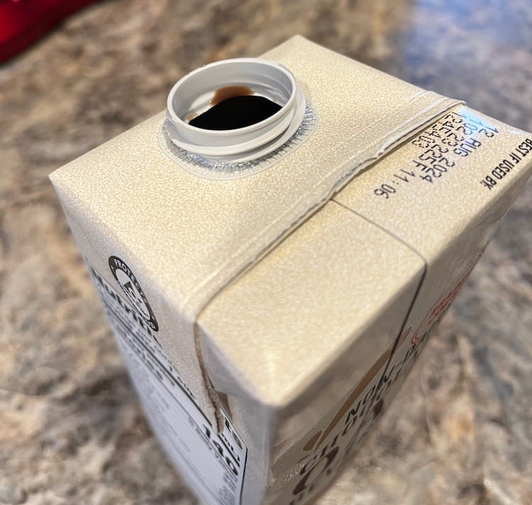 Photo of the opening of a cardboard beverage container showing dark brown liquid on the rim.