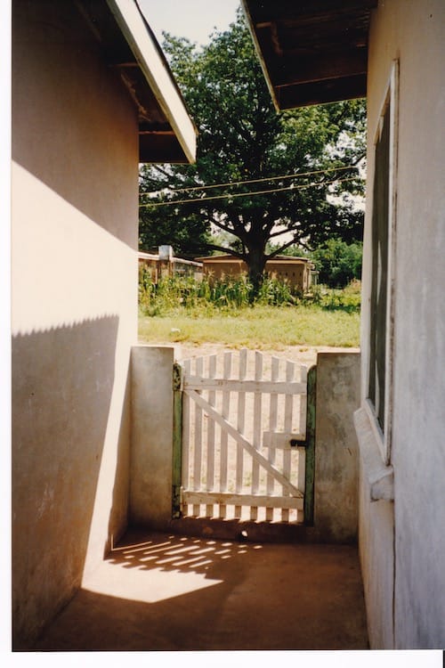 Africa_gate Photo of a white gate and beyond it a small plot of grass leading up to maize plants and more bungalows
