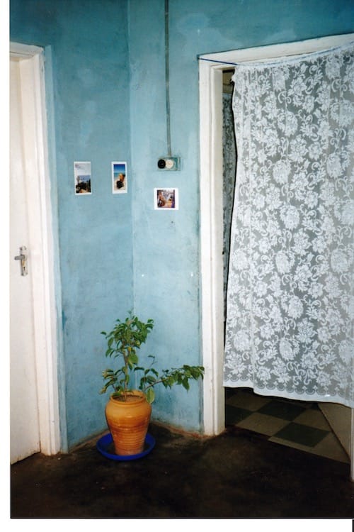 Africa_lace Corner of room showing open doorway to the right covered with a lace curtain. A green plant in a terracotta pot is in the corner. Walls are a washed out blue.