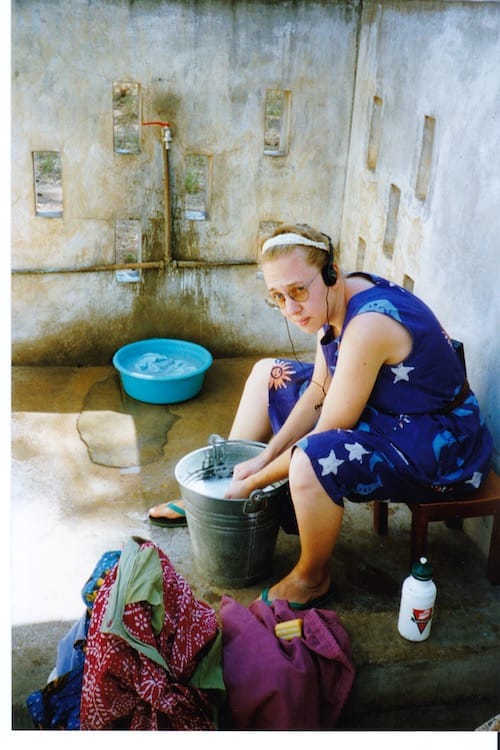 Africa_washing_clothes Photo of Vanessa Kier looking less than thrilled while sitting on a stool washing clothes in a five gallon bucket in the washing area by her outdoor faucet.
